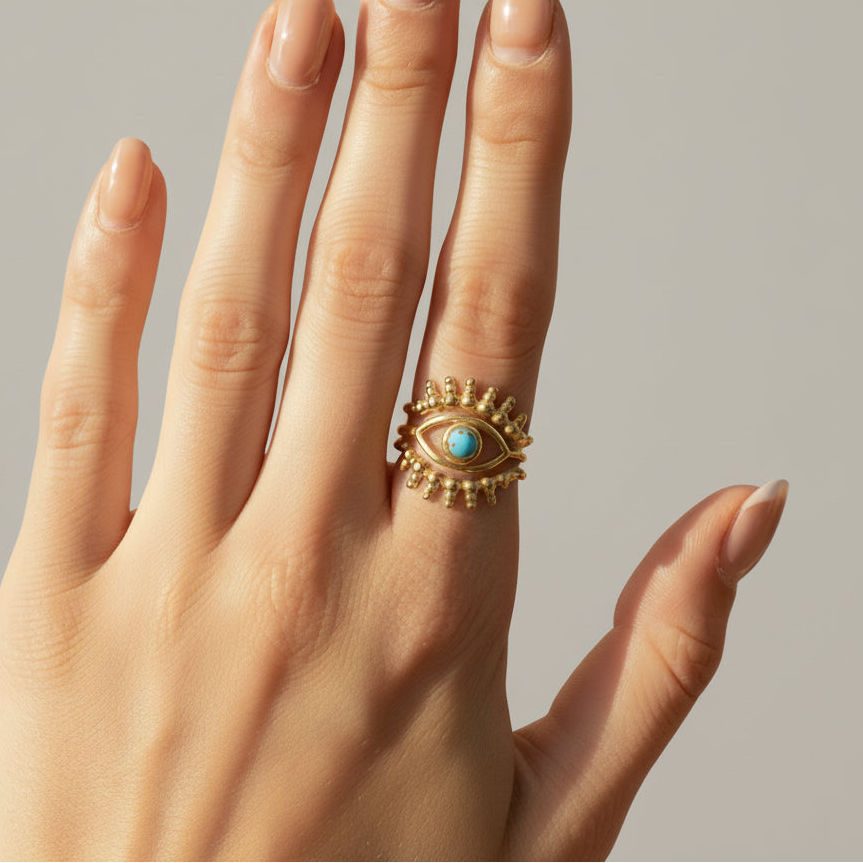 Hand wearing a gold ring with a turquoise stone on a textured surface