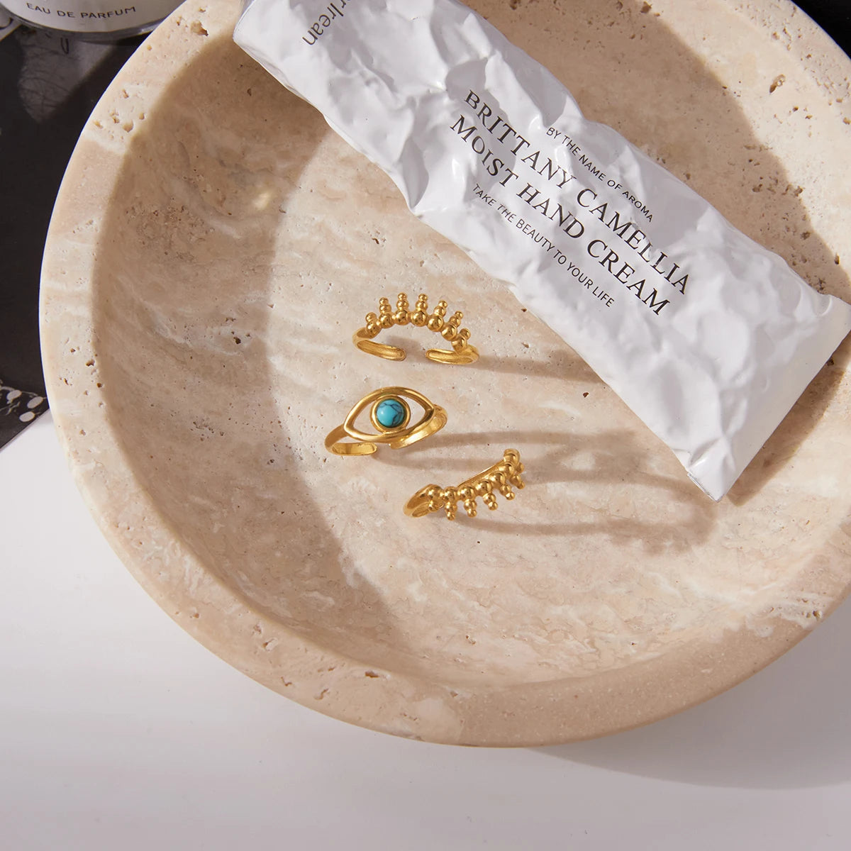 Three gold rings on a beige plate with a white tube of hand cream.